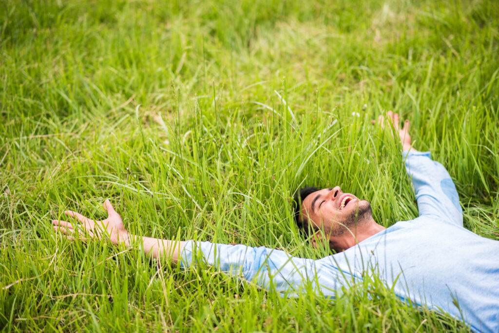 Happy pretty man lying on the green grass with arms outstretched